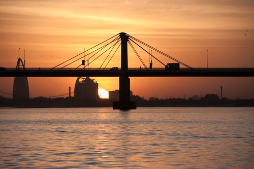 Free Silhouette of a bridge against a vibrant sunset sky reflecting on a calm body of water. Stock Photo