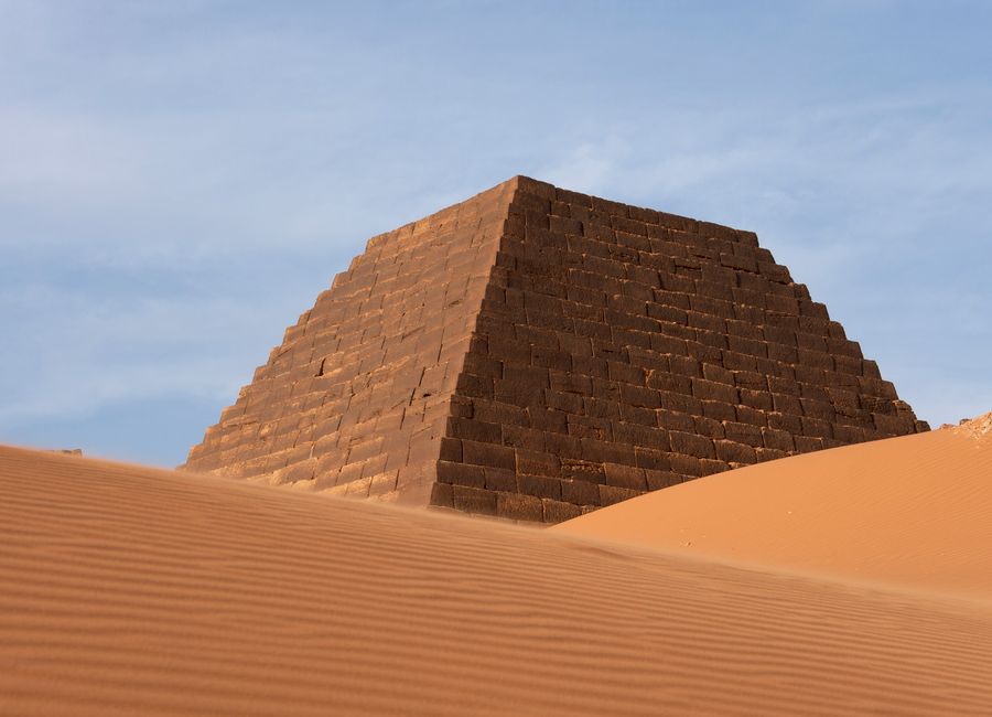 A striking image of an ancient pyramid amidst desert dunes under clear blue skies.