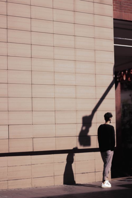 Free A man stands against a tiled wall, casting a shadow in urban sunlight. Stock Photo
