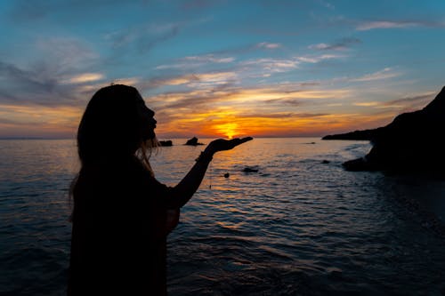 Silhouette of Woman Standing on Seashore during Sunset