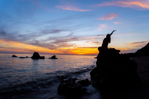 Silhouette of a Woman Sitting on a Rock During Sunset
