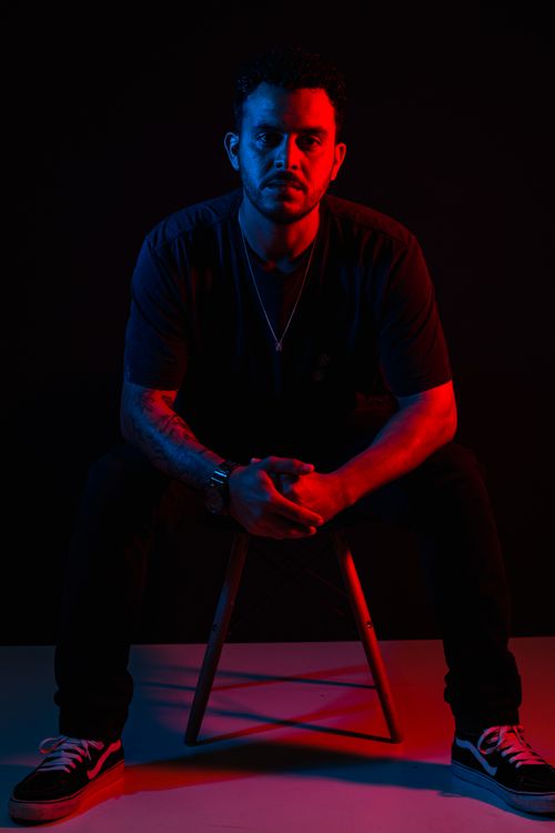 Free A dramatic portrait of a man sitting on a stool with red and blue lighting effects. Stock Photo