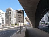 Contemporary bus stop sign on a city street in Doha, Qatar, featuring modern architecture.