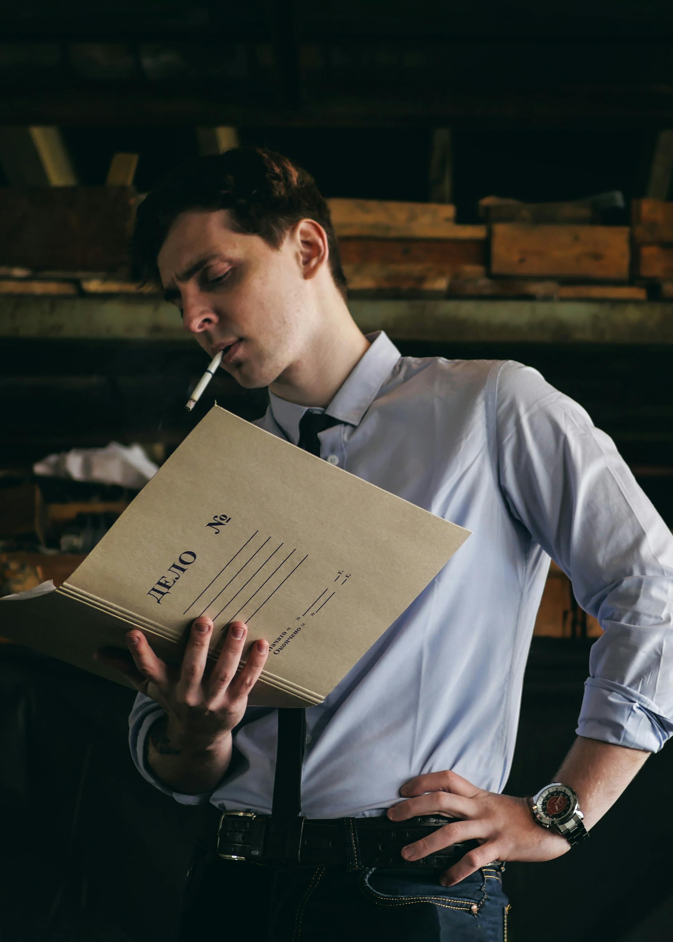 A thoughtful detective smoking while reviewing case files inside a dark room.