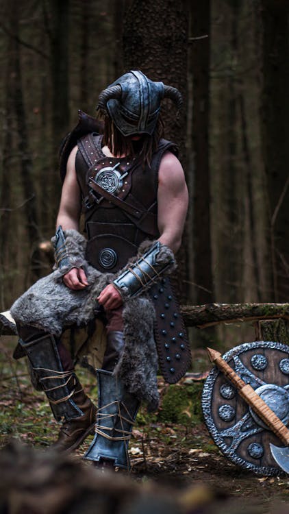 Un hombre con una armadura vikinga se para en un bosque.