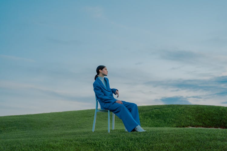 Woman In Blue Suit Sitting On Chair On Grass Field