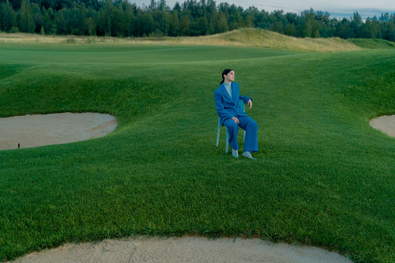 Woman in a blue suit seated on a chair in the middle of a golf course