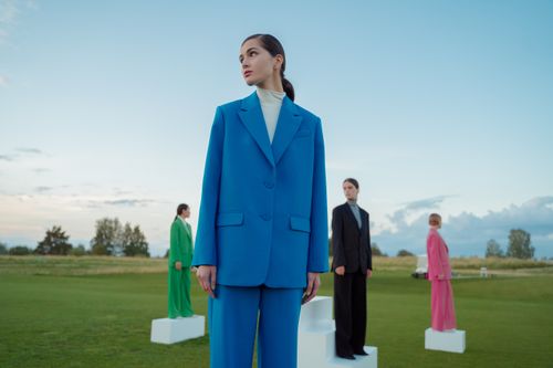 Free Four women in colourful suits standing on grass under a blue sky, posing artistically. Stock Photo