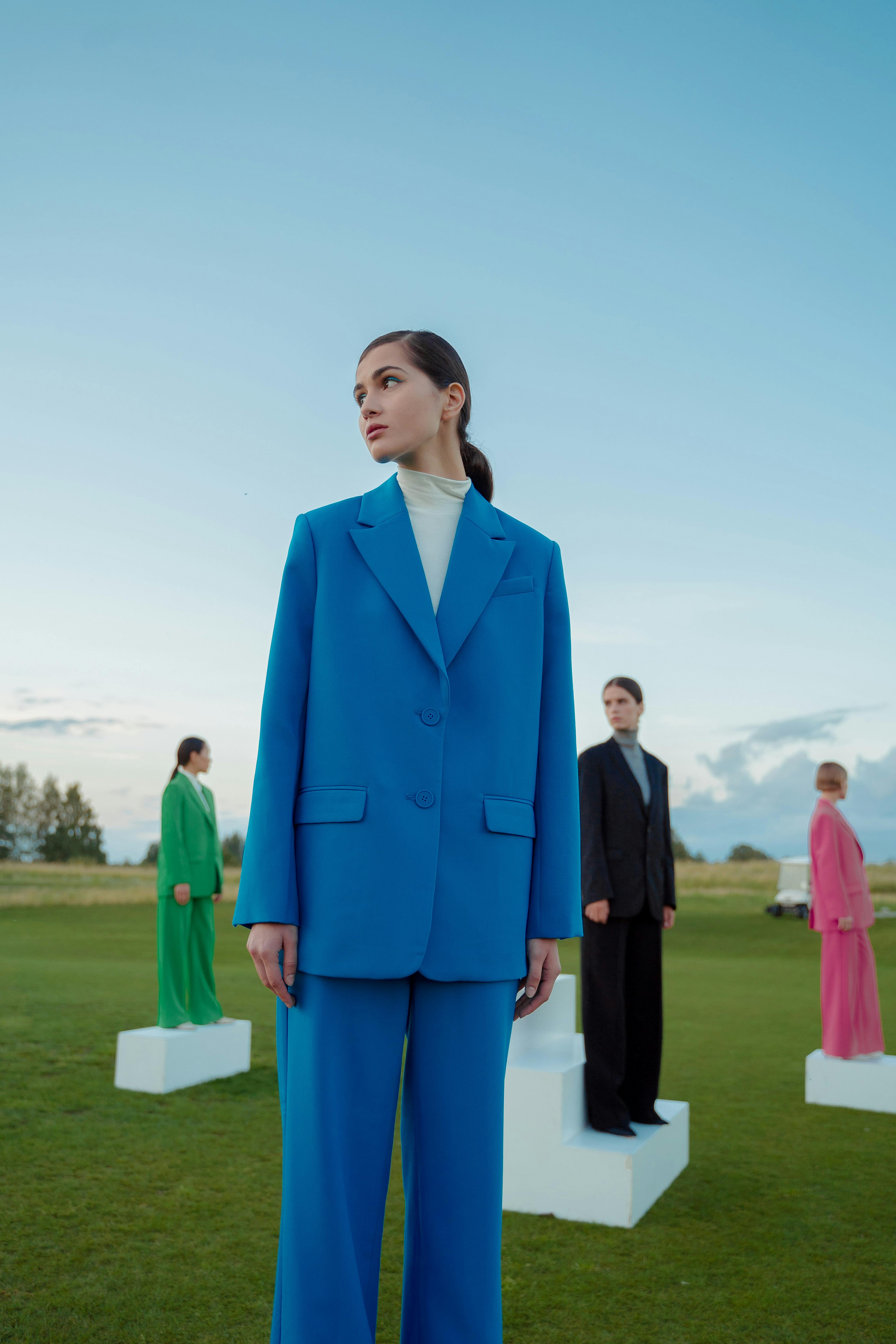 Fashionable women posing in diverse colorful suits on a grass field.