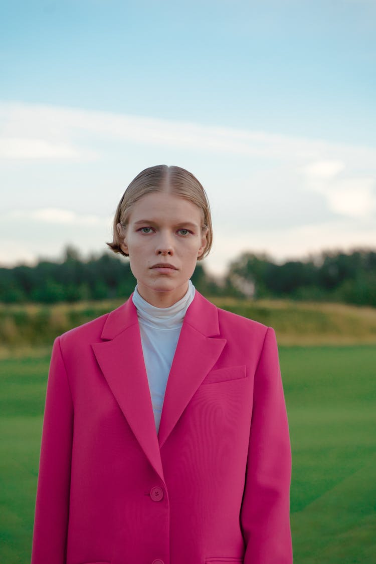 Woman In Pink Blazer Standing On Grass Field