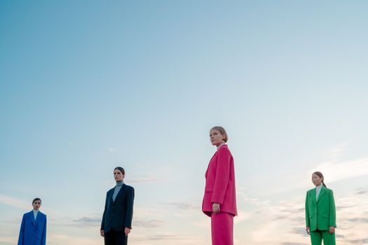 Four fashion models in colorful suits standing outdoors under a clear blue sky.