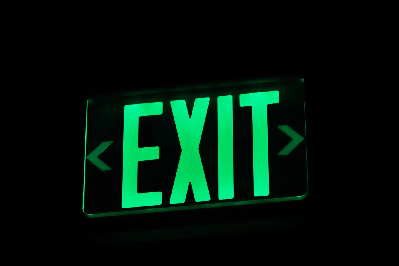 Bright green exit sign illuminated in darkness, indicating direction.