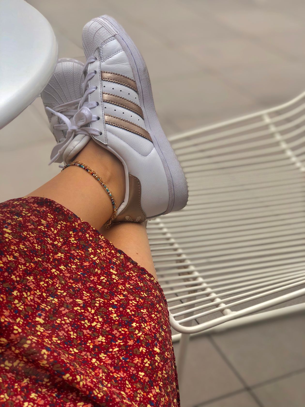 Close-up of white sneakers with gold stripes worn with a red floral skirt and beaded anklet.