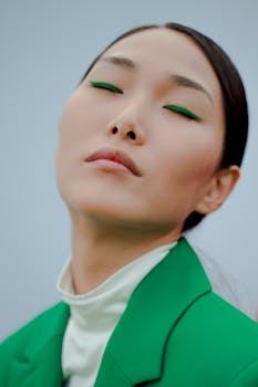 Close-up of an Asian woman with green eyeshadow and a green suit, eyes closed in serene expression.