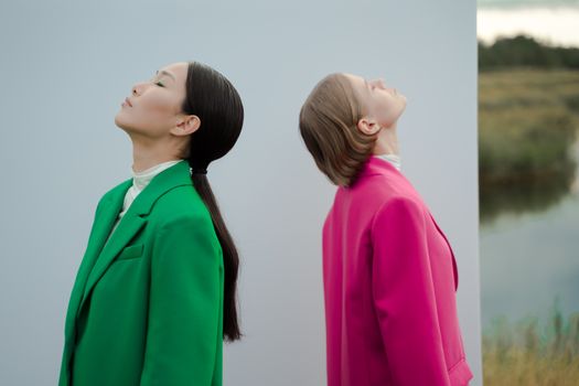 Elegantly dressed women posing outdoors in vibrant colored blazers with a serene backdrop.