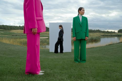 Free Models in colorful suits pose creatively on a grassy field beside a lake under a dramatic sky. Stock Photo