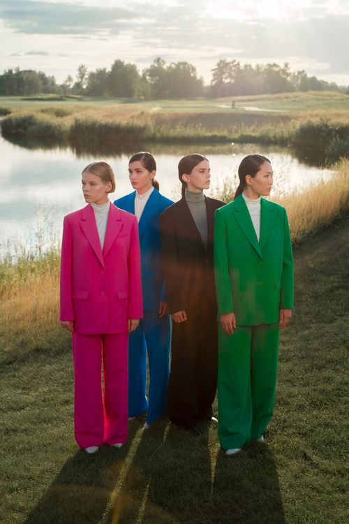 Free Four elegantly dressed women in colorful suits posing by a serene lake. Stock Photo