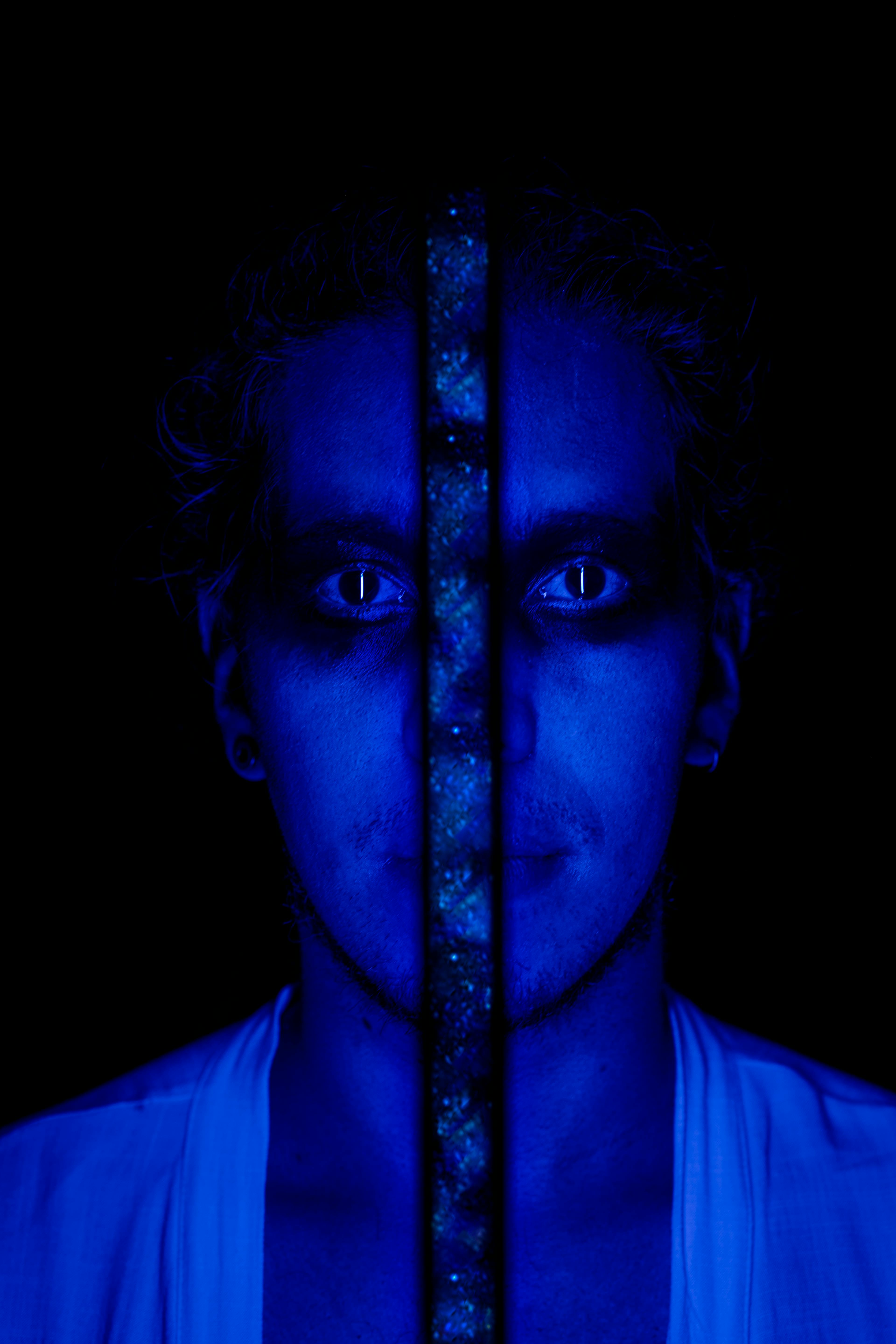 Free Portrait of a man with art makeup in blue lighting, conveying a mysterious and eerie mood. Stock Photo