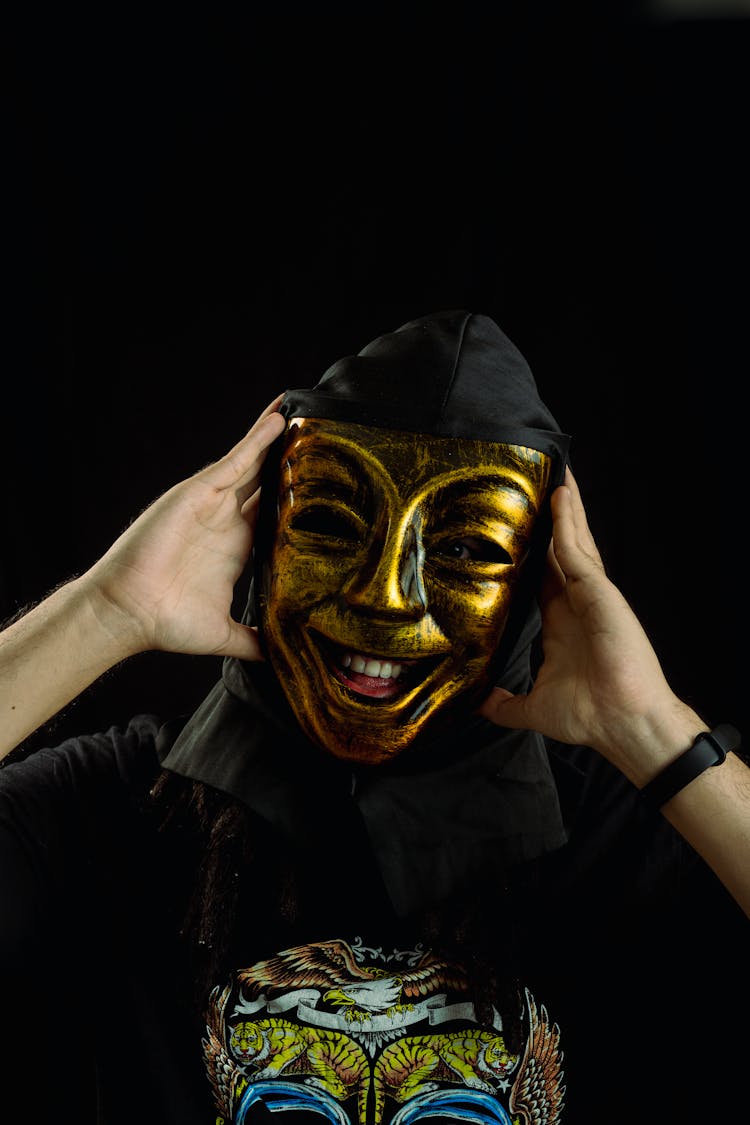 Close-Up Shot Of A Person Wearing Gold Mask On Black Background