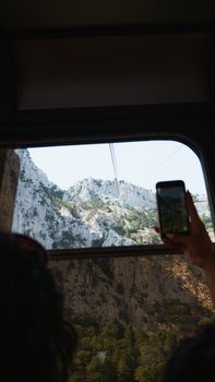Capture of mountains through a train window with a phone in hand.