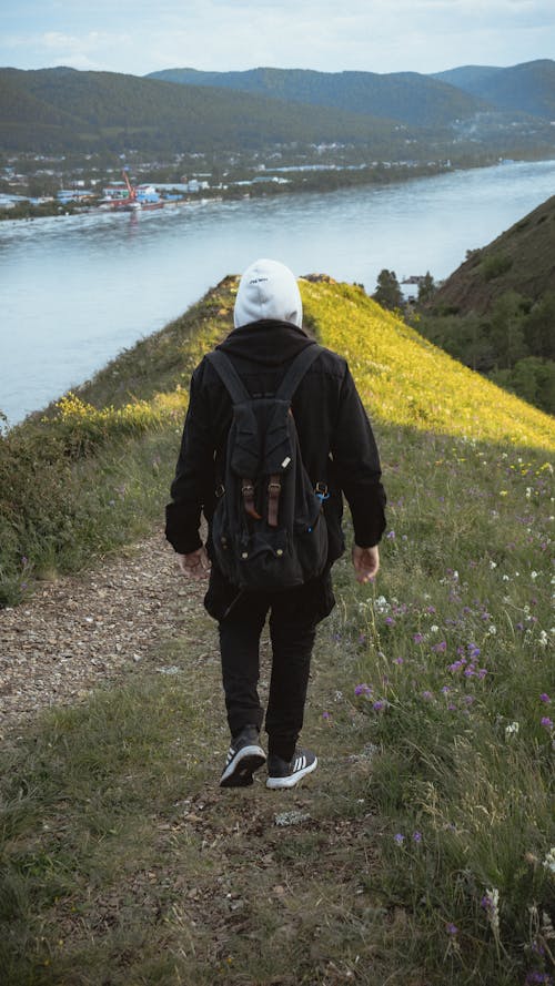 Back View of a Man with a Backpack Walking on Grass