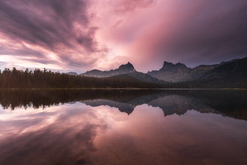 Free Body of Water Near Green Trees and Mountain Under Cloudy Sky Stock Photo