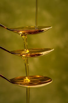 Artistic capture of honey pouring over stacked spoons with a green background.
