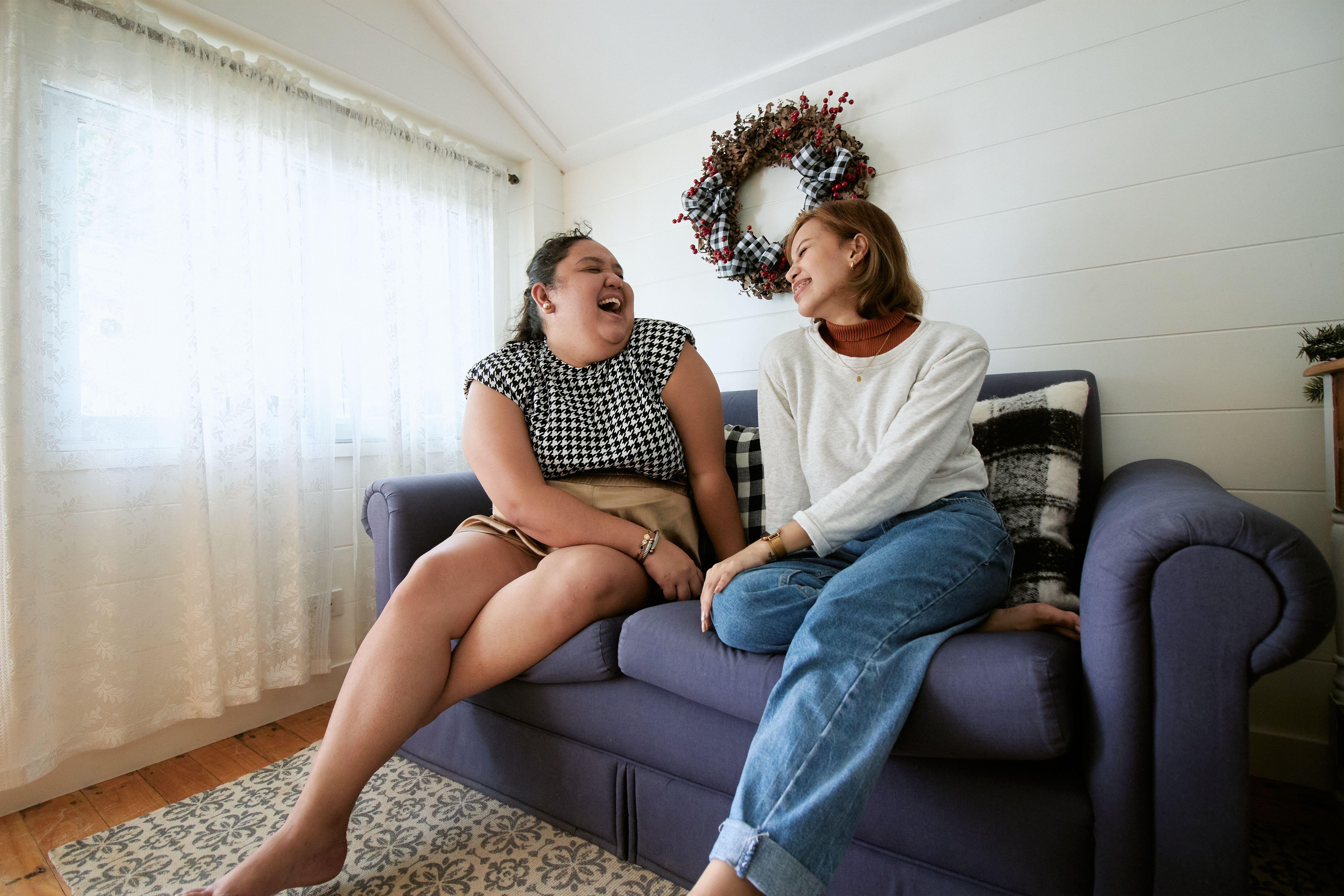 Two women sitting on a sofa at home, sharing laughter and enjoying each other\'s company.