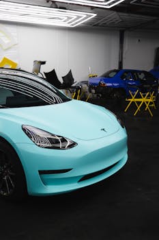 Modern turquoise Tesla car parked in a garage with overhead lights.