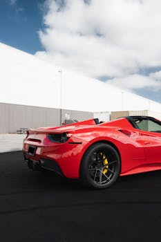 Luxury red sports car parked outdoors under a blue sky with clouds.