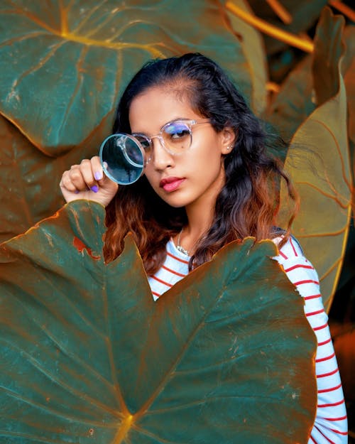 A Woman Holding a Magnifying Glass Behind a Big Leaf