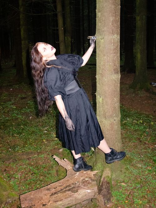 Free A gothic woman in a black dress poses dramatically by a tree in a lush Moscow forest. Stock Photo