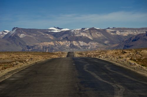 Free A vast arid landscape with a road leading to snow-capped mountains under a clear blue sky. Stock Photo