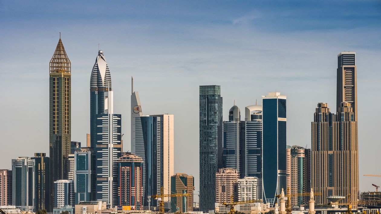 Panorámica del skyline de Dubai al atardecer con los rascacielos del centro financiero reflejados en el agua, vista desde la orilla de la bahía.