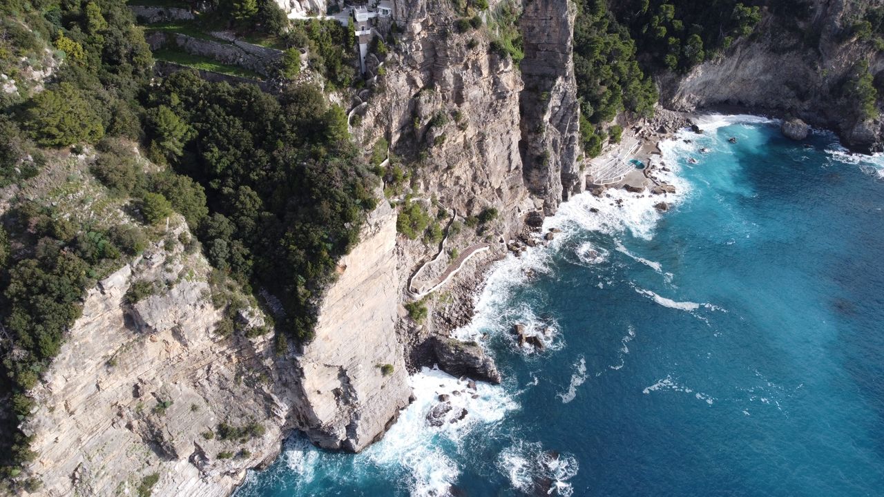A narrow footpath traversing a sheer cliff high above the turquoise water of the Amalfi Coast in Italy