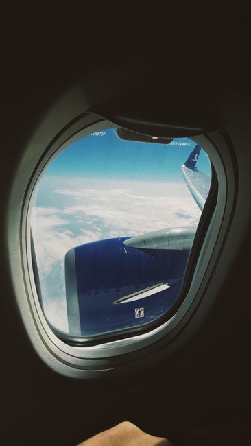 View of an airplane engine through a window above the clouds, showcasing travel and aviation.