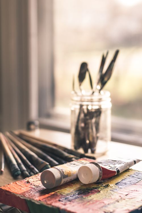 Free Close-up of paint tubes and brushes on a table by the window in warm lighting. Perfect for creative themes. Stock Photo