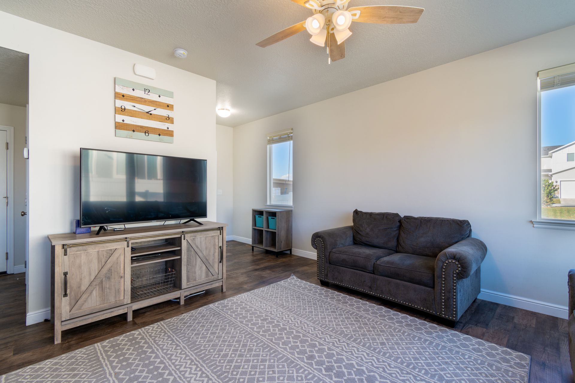 Spacious modern living room featuring a cozy sofa, TV stand, hardwood flooring, and ceiling fan.
