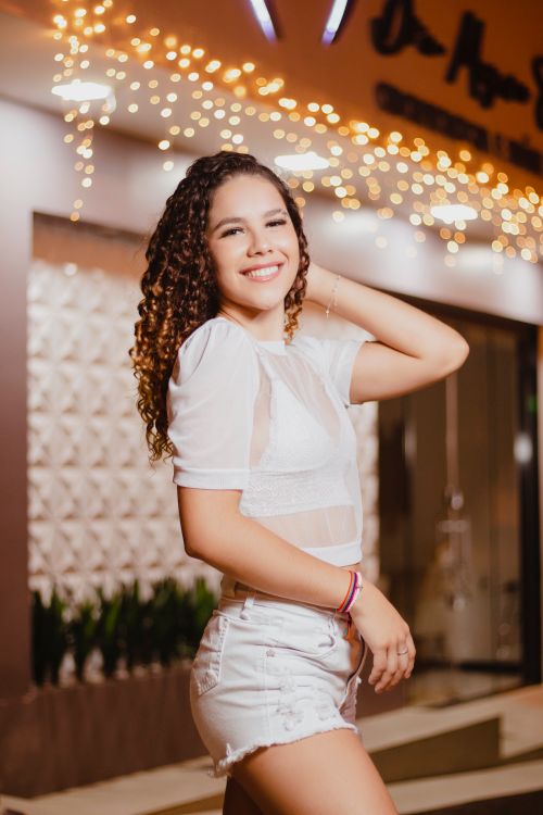 Free A smiling woman with curly hair wears white attire and poses confidently outdoors at night. Stock Photo