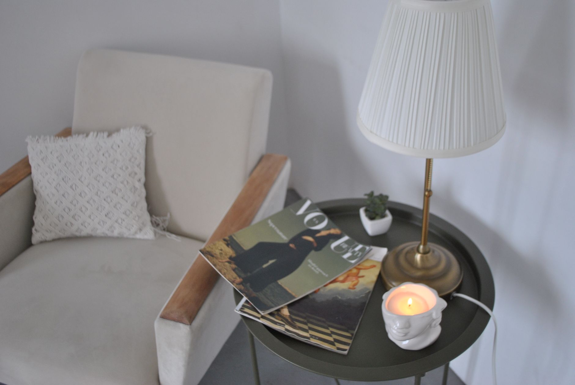 Elegant living room corner featuring an armchair, magazines, and a candlelit table for a relaxing ambiance.