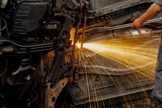 Mechanic welding car engine parts, with bright sparks flying. Hands-on automotive repair scene in workshop.