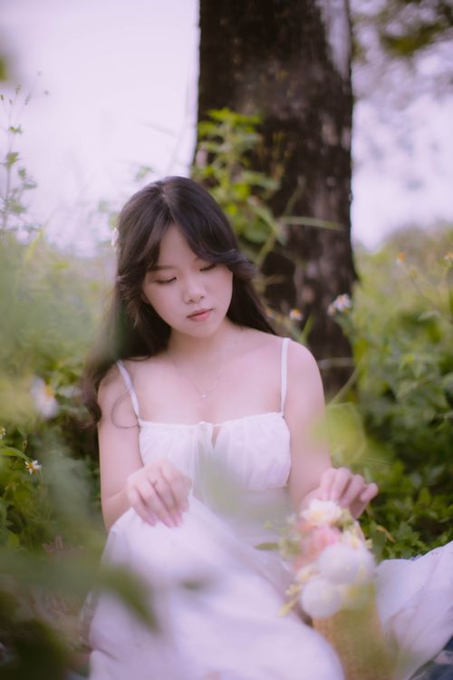 Free A serene portrait of a young woman in a white dress surrounded by summer flowers in a lush garden. Stock Photo