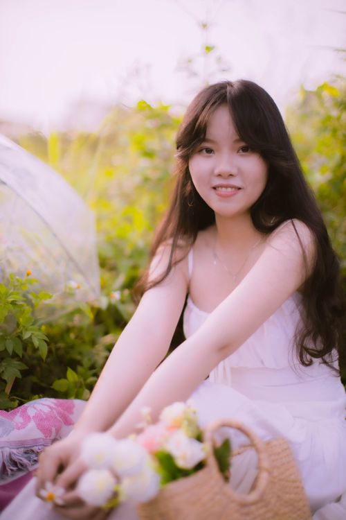 Free A young Asian woman sitting in nature, smiling while enjoying a sunny day. Stock Photo