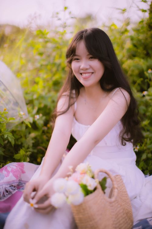 Free A young woman smiling in a garden, holding a woven basket with flowers. Stock Photo