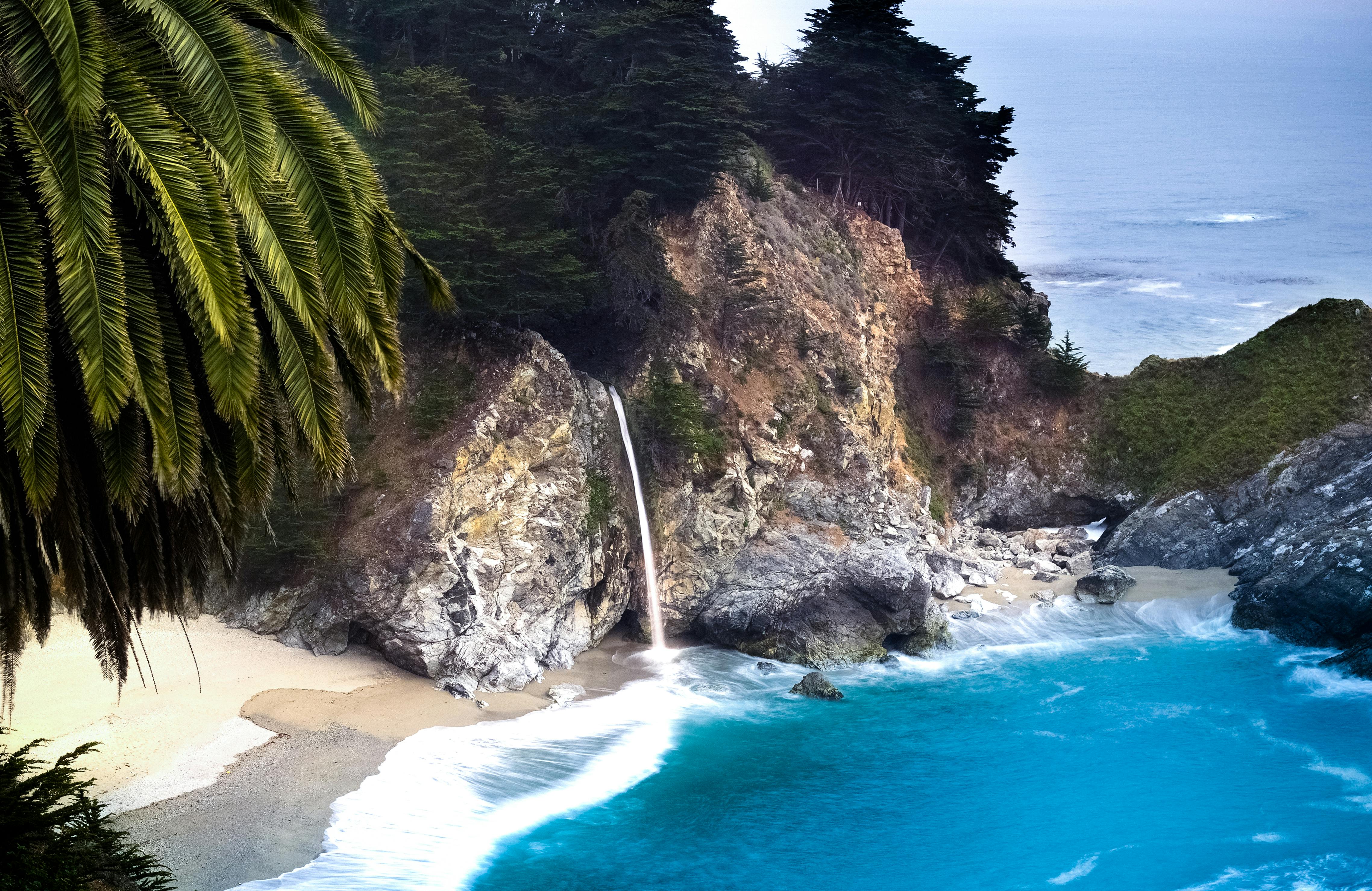 Blue Sea Near Brown and Grey Rock With Green Leaf Trees · Free Stock Photo