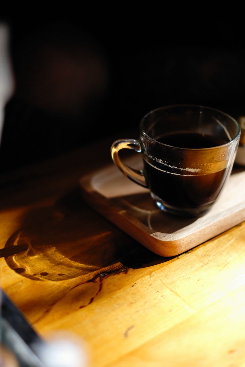 Café negro en taza de vidrio sobre tabla de madera
