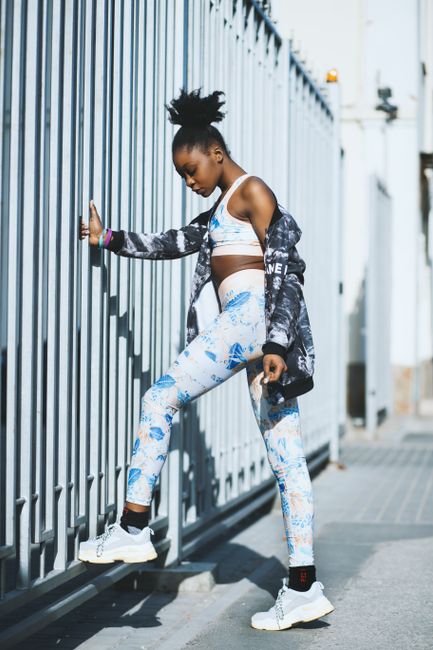 Young black woman exercising outdoors, dressed in modern fitness wear, showcasing urban workout fashion.