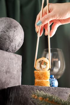Close-up of sushi rolls held with chopsticks, against a geometric background.