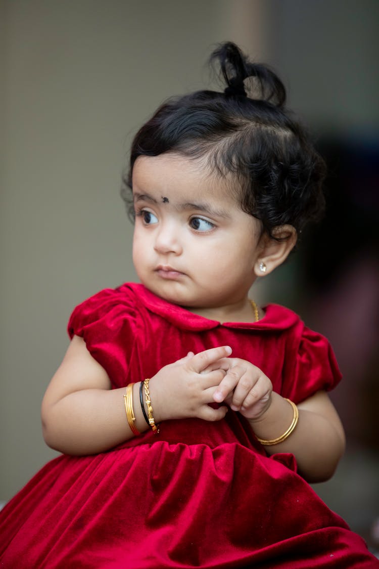 A Cute Baby Girl In Red Dress Wearing Gold Bangles