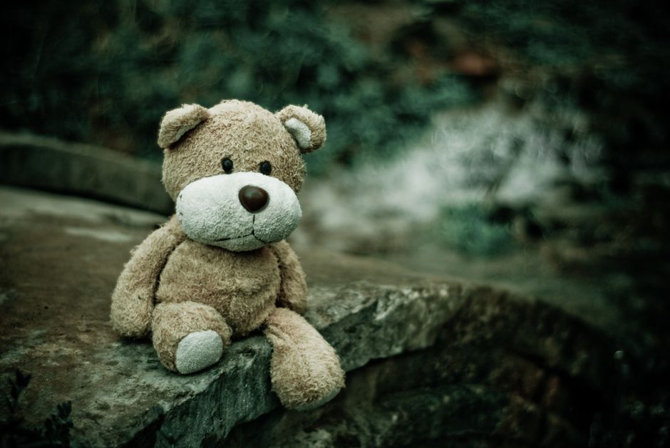 A plush teddy bear sits alone on a stone wall, evoking a sense of nostalgia and loneliness.